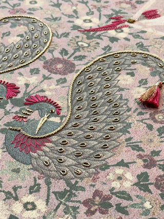 A detailed macro close-up of the Kashmiriyat embroidered wall art highlighting a peacock worked in gold thread on a blush floral ground.
