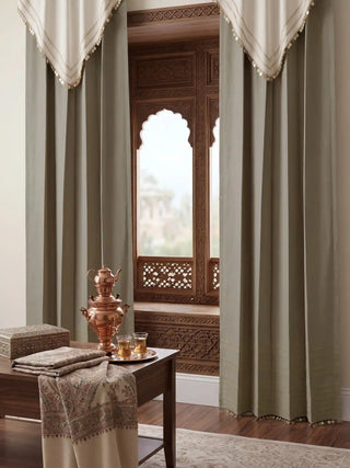 Full-length view of a sage green Kashmiriyat curtain with an ivory valance and gold coin fringe against a neutral wall.