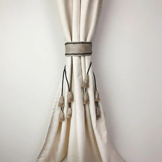 Kaya Handcrafted Curtain Tieback secured around a cream curtain, showing the jute fabric panel and multiple hanging tassels.