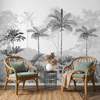 Kovalam monotone tropical wallpaper in grey with tall palms and banana leaves behind two rattan armchairs and a wire side table on a jute rug