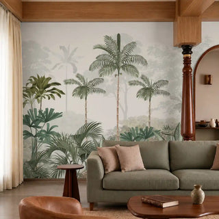 Kovalam tropical wallpaper in green with layered palms and misty forest behind an olive sofa and carved wooden column in a living room