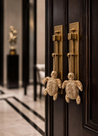 The Kurma charm in Gold, view-doorpulls hanging in a matching pair from brass entry door handles.