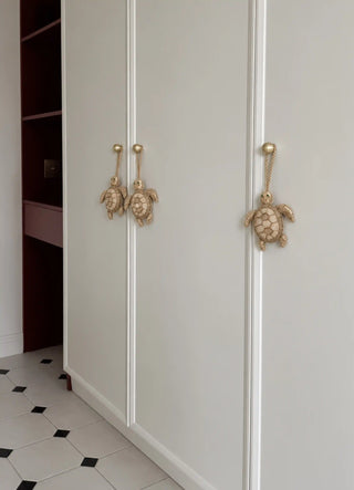 The Kurma charm in Gold, view-wardrobehandles hanging in a set of three on wardrobe doors.
