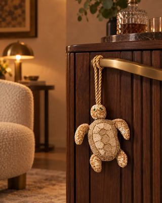 Kurma gold embroidered turtle charm hanging from an antique brass ring pull on a carved walnut armoire.