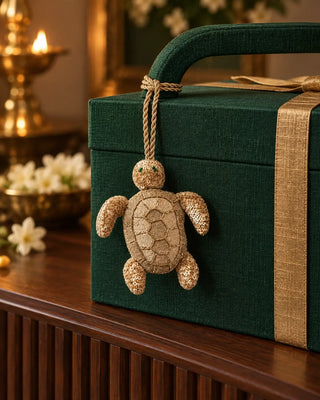 Kurma gold embroidered turtle charm tied to an emerald green gift box handle