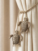 A close-up of hand-embroidered golden turtle charms with champagne sequins on a braided silk rope.