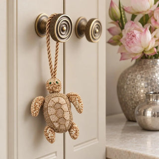 A detailed macro close-up of the Kurma Turtle Gift Charm highlighting its beaded shell, sequinned flippers and twisted gold cord on a brass-toned knob.