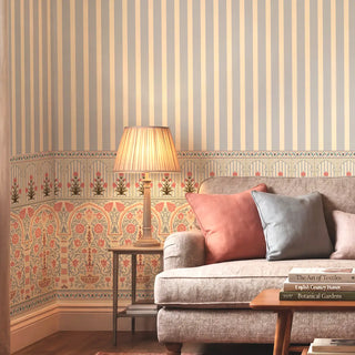 A luxury living room featuring the Kusum wallpaper with Mughal arches and vertical stripes behind a plush beige sofa.