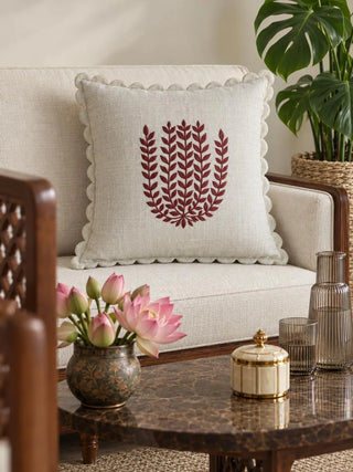 Leafora cushion cover on a cream sofa with a dark wood frame, beside a marble-topped table with pink lotus flowers in a patterned bowl, a ribbed smoky glass carafe and a cream and gold lidded box.