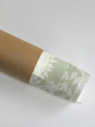 A close-up of the Geet Madhubani sage green artwork showing the intricate white sun and bird motifs as it is unrolled from a premium shipping tube.