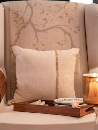 The Linen Poet cushion cover in cream with an open-weave mesh panel and tan stitched edging, styled on a wingback chair.