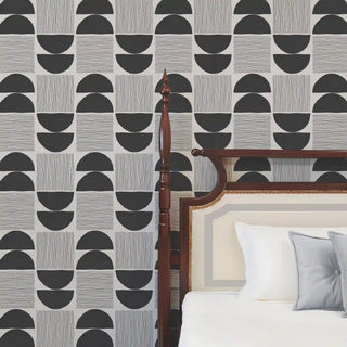A modern bedroom featuring the Luna Stripe charcoal and bone geometric wallpaper behind a classic dark wood bed frame.