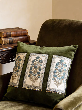 The Nayab olive green embroidered cushion styled in a warm heritage interior next to a botanical wall.