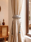 The Cloud Loom curtain tie back styled in a sunlit lounge next to a natural oak window frame and mid-century console table.
