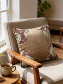 The Rustic Frame embroidered velvet cushion styled on a modern light-grey armchair.
