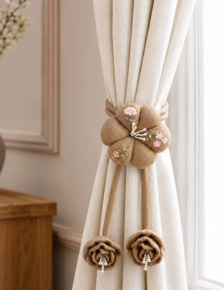 The Petal Knot curtain tie back styled elegantly on an ivory curtain panel, showing the beautifully draped rose tassels hanging below.