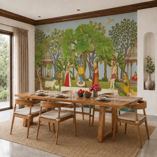The Madhuban Vihar wallpaper mural in Sage & Sky Blue installed on a feature wall in a dining room, depicting Krishna with gopis, a peacock, cows and chattri pavilions behind a wooden dining table. view-dining