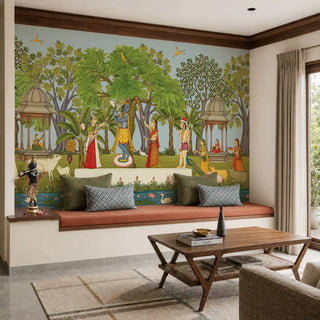 The Madhuban Vihar wallpaper mural in Sage & Sky Blue installed on a feature wall in a living room, depicting Krishna with gopis in a forest garden with cows, a lotus pond and chattri pavilions, above a built-in seating bench. view-livingroom