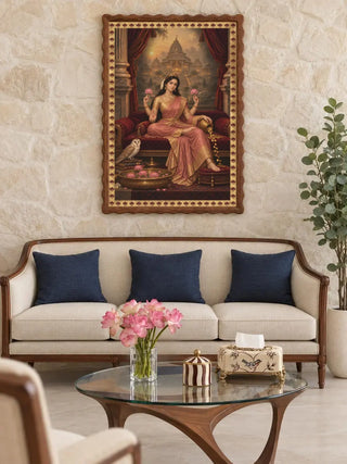 The Mahalakshmi Darbar wall art in a wavy walnut frame on a stone wall above a cream sofa with navy cushions and a glass coffee table.