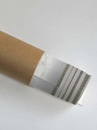 A close-up of The Malabar Wall Art in Mist-Grey rolled and packaged in a protective shipping tube, showing the decorative dentil border edge.