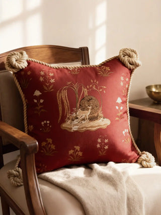 A luxury Malhar Rustic Corner cushion featuring crimson heritage motifs and knotted rope corners on a vintage chair.