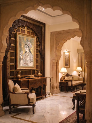 Malika-e-Riyasat wall art in a gilt frame set against a carved wooden arch above a console with brass vessels in a marble-floored foyer