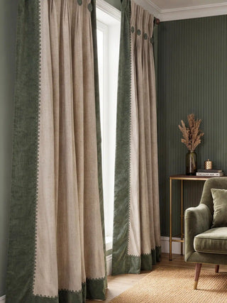 A pair of Manika curtains framing a window in a sophisticated room with fluted green walls and velvet furniture.