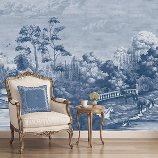 A blue European vintage wallpaper depicting a manor estate scene with trees, a stone bridge, and horses, displayed behind an elegant armchair and side table.