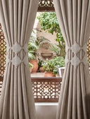 Symmetrical styling of the Marrakesh Moti architectural tiebacks gathering drapes flanking a window that overlooks a Moroccan riad courtyard.