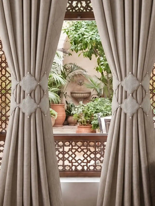 Symmetrical styling of the Marrakesh Moti architectural tiebacks gathering drapes flanking a window that overlooks a Moroccan riad courtyard.