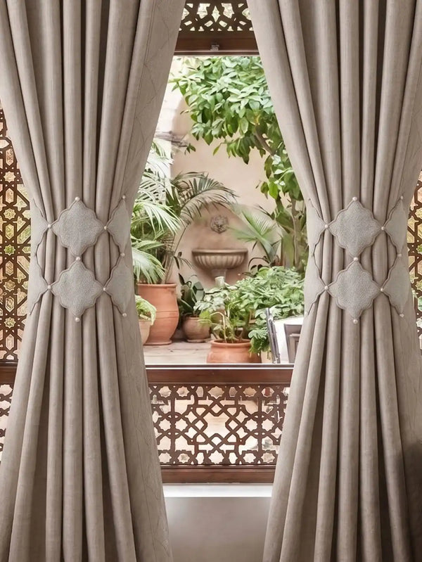 Symmetrical styling of the Marrakesh Moti architectural tiebacks gathering drapes flanking a window that overlooks a Moroccan riad courtyard.