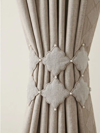 A detailed macro view of the Marrakesh Moti trellis tie back gathering a heavy greige linen curtain panel into architectural folds.
