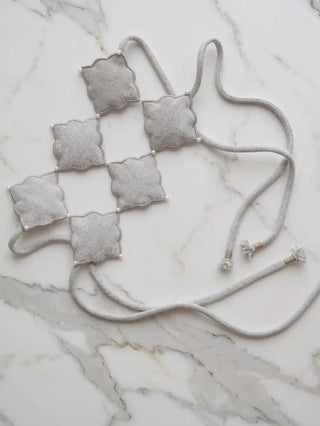 A flat lay view of the Marrakesh Moti curtain tie back against marble, showcasing the full layout of the interlocking ogee trellis and loops.