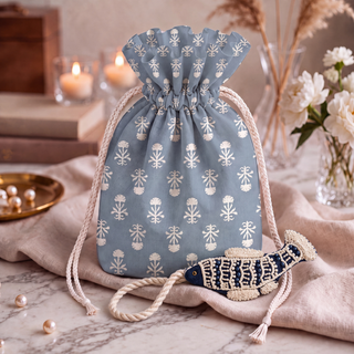 The Matsya Fish Charm in Navy & Ivory styled beside a dusty blue potli bag printed with a repeating stemmed floral motif.