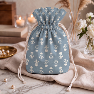 Close view of the dusty blue potli bag's stemmed floral print, paired with pearls and candles on marble.