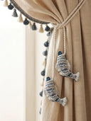 Hand-embroidered indigo fish charms with silver sequins holding back cream linen curtains with tassel trim.