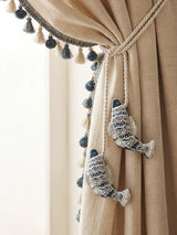 Hand-embroidered indigo fish charms with silver sequins holding back cream linen curtains with tassel trim.