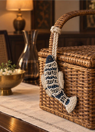 A hand-beaded Matsya fish charm in navy and ivory, pearl beads and sequins worked in scale-pattern rows, tied by rope to the handle of a woven rattan basket