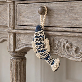 The Matsya Hanging Gift Charm in navy and ivory hanging from a brass knob on a distressed grey-wood console drawer.