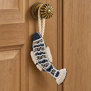 The Matsya Hanging Gift Charm in navy and ivory hanging from a fluted brass door knob on a honey-toned panelled wooden door.