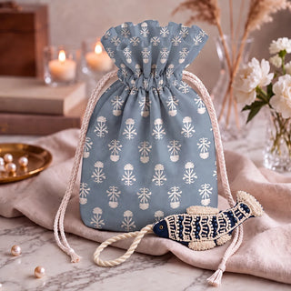 The Matsya Hanging Gift Charm in navy and ivory resting beside a dusty blue drawstring pouch printed with white floral motifs.