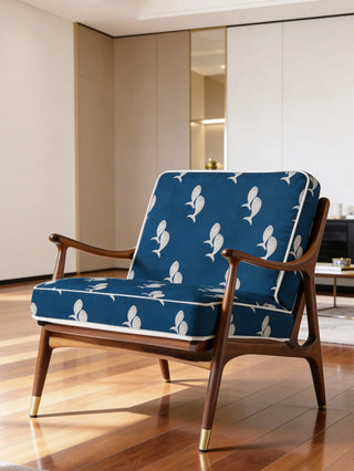 A luxury mid-century armchair upholstered in Meen navy blue fabric with white fish motifs and white piping.