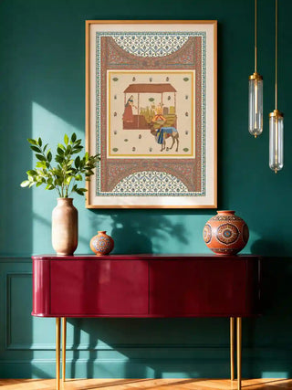 Meena Bazar wall art in ivory and terracotta, framed in pale gold on a deep teal wall above a burgundy console with painted pots and brass pendant lights in an entryway.