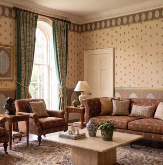 Meena Buti wallpaper in parchment, terracotta and teal applied across the walls of a classical drawing room with brown floral sofas, teal curtains, a marble coffee table, Persian rug, and arched sash window — showing the full three-part scheme with oval cornice border and arch dado