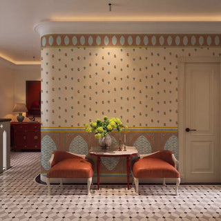 Meena Buti wallpaper in parchment with terracotta oval cornice border and teal arch dado applied on a curved wall in a contemporary Indian interior, styled with two terracotta upholstered chairs, a red pedestal table with yellow flowers, and geometric black and white floor tiles