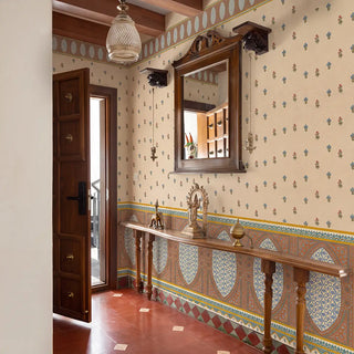 Meena Buti wallpaper in parchment covering the walls of a traditional Indian heritage foyer with dark walnut door, terracotta diamond floor tiles, a wooden console shelf with brass deity figurines and elephant, crystal pendant light, and carved walnut framed mirror