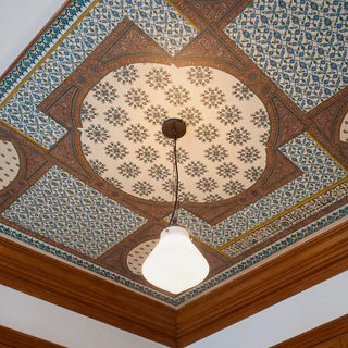 Close-up of Meena Jaal ceiling mural showing the central parchment medallion field of rotating crimson and pale blossom bouquet clusters, surrounded by terracotta arched borders and teal arabesque jaal panels, with a pendant light at centre