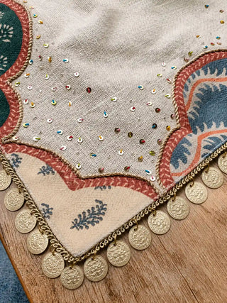 A detailed close-up view of the brick-red piped border, block-printed leaf strips, and hanging metallic coin accents on the Mehrab mat.