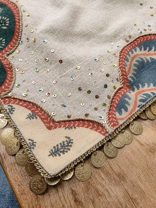 A detailed close-up view of the brick-red piped border, block-printed leaf strips, and hanging metallic coin accents on the Mehrab mat.