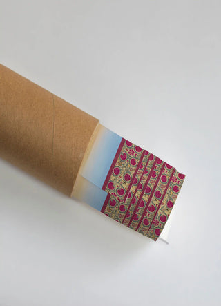 The Mewar wall art print partially unrolled from its kraft paper shipping tube, showing a blue-to-peach ombre gradient panel beside a floral medallion scroll pattern in magenta, teal and cream.